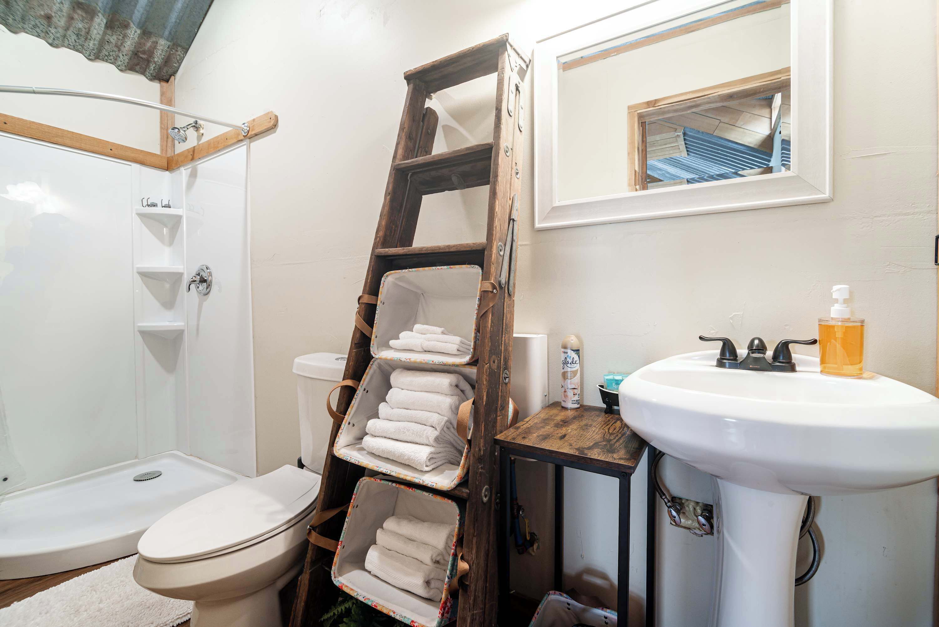 Ein Badezimmer mit Dusche, Toilette, Waschbecken und einer Holzlade mit Handtüchern.