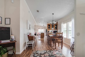 A spacious kitchen with wooden cabinets, a dining table, and chairs. There is a chalkboard on the wall and a rug on the floor.