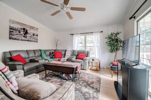A living room with a sectional sofa, a coffee table, a TV, and a ceiling fan.