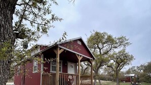 A rustic cabin with a porch, surrounded by trees and a gravel path. - Hill Country Cabin 3 | Sleeps 4, Gas Grill (Canyon Lake)