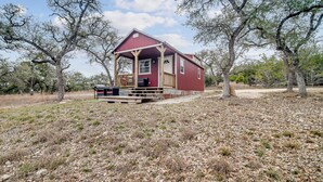 A red wooden house with a porch, surrounded by trees and dry grass. - Hill Country Cabin 3 | Sleeps 4, Gas Grill (Canyon Lake)