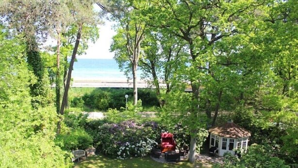 Un exuberante jardín con un pabellón, un banco y vistas al mar.