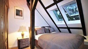 Un dormitorio con techo inclinado, una cama con cubrecama gris, una mesita de noche con lámpara y un cuadro enmarcado en la pared.