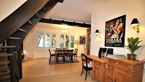 Amplia sala de estar con mesa de comedor, sillas, una escalera y área de cocina con armarios y una cafetera.