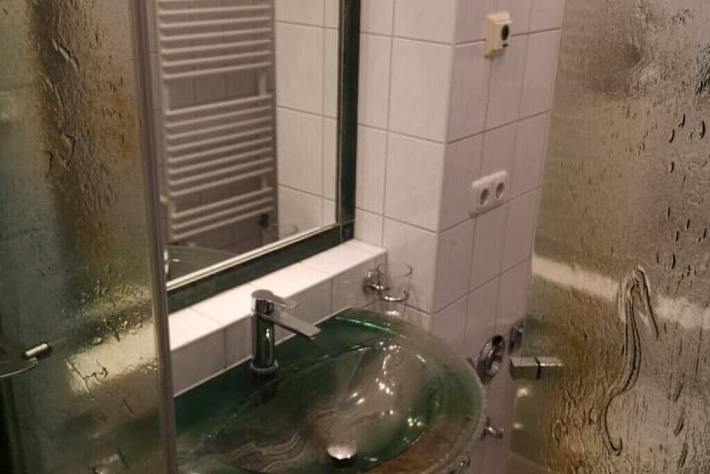 A bathroom with a glass sink, a mirror, and tiled walls.