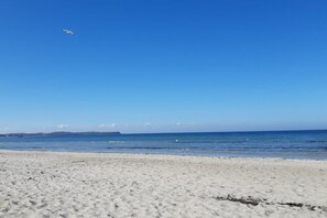 Una playa con cielo despejado y un barco a lo lejos.