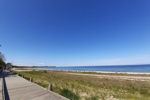 Une promenade en bois qui mène à une plage, avec un ciel bleu dégagé.