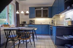 Une cuisine de taille réduite avec des meubles bleus, une table à manger avec des chaises, un four à micro-ondes et une machine à café.