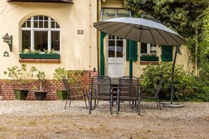 Een terras met een tafel, stoelen, een parasol en potplanten.