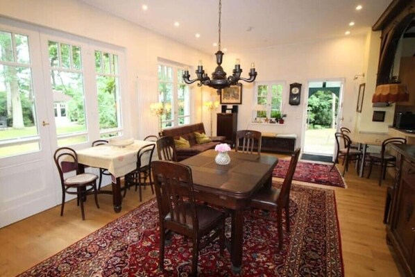 Een eetruimte met een houten tafel en stoelen, omringd door grote ramen en een kroonluchter.