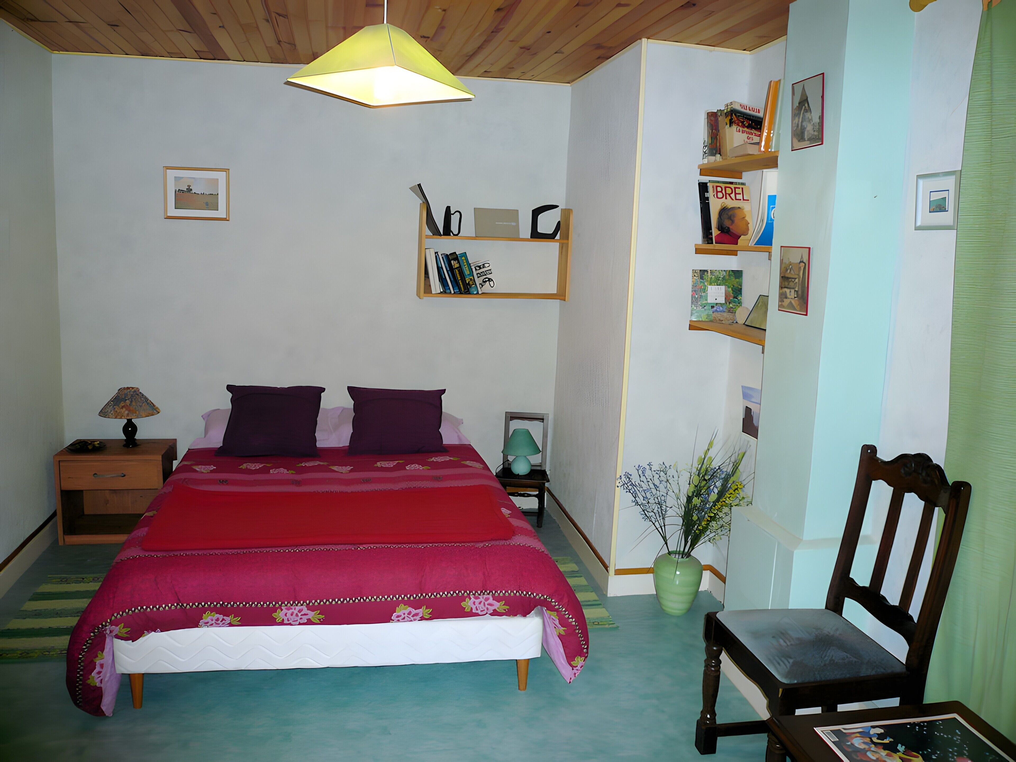 Une chambre à coucher comprenant un lit, une table de chevet, une lampe, une chaise, une bibliothèque et un luminaire suspendu.