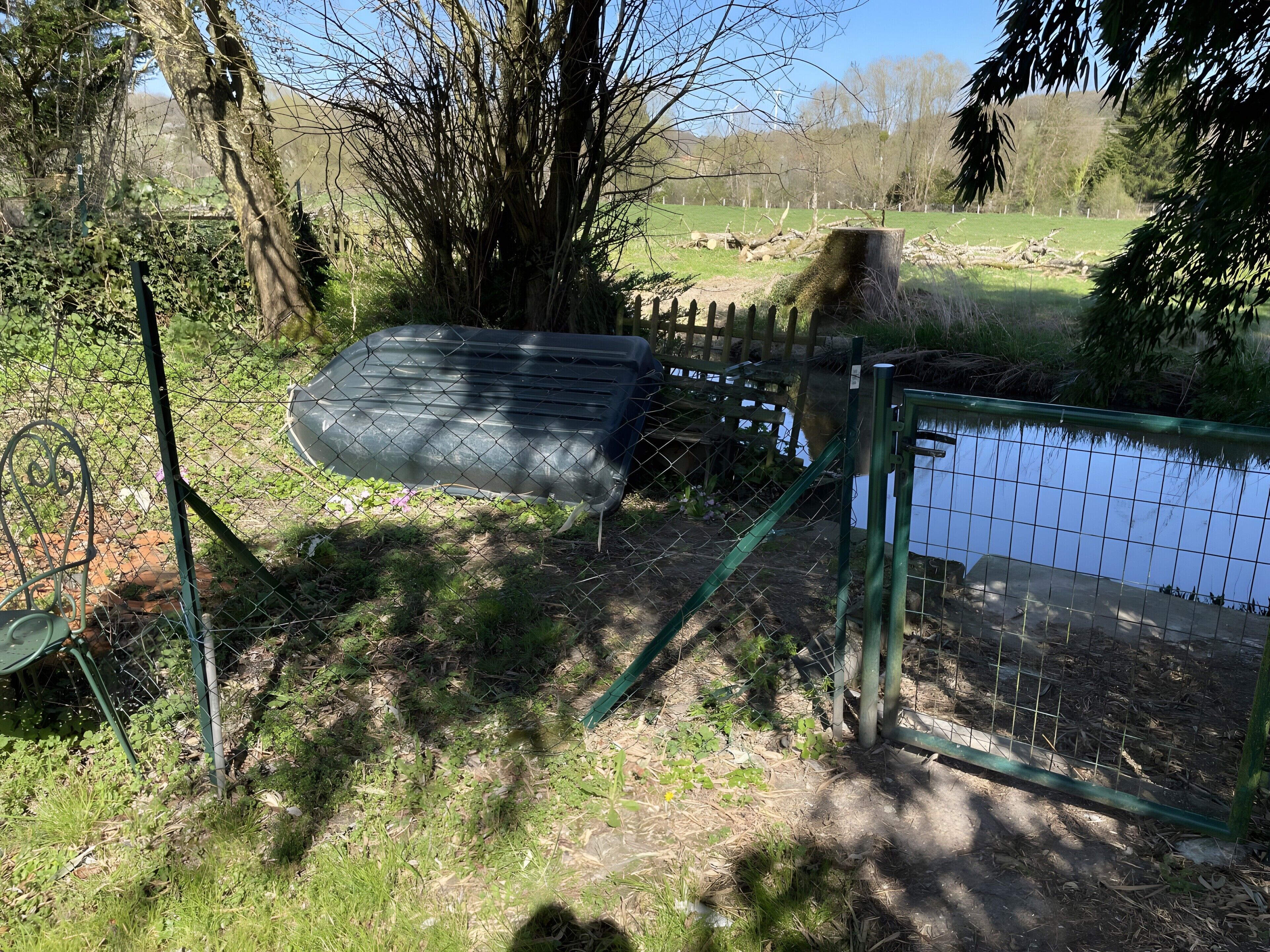 Een omheind buitengebied met een vijver, een grote boom en een metalen constructie.
