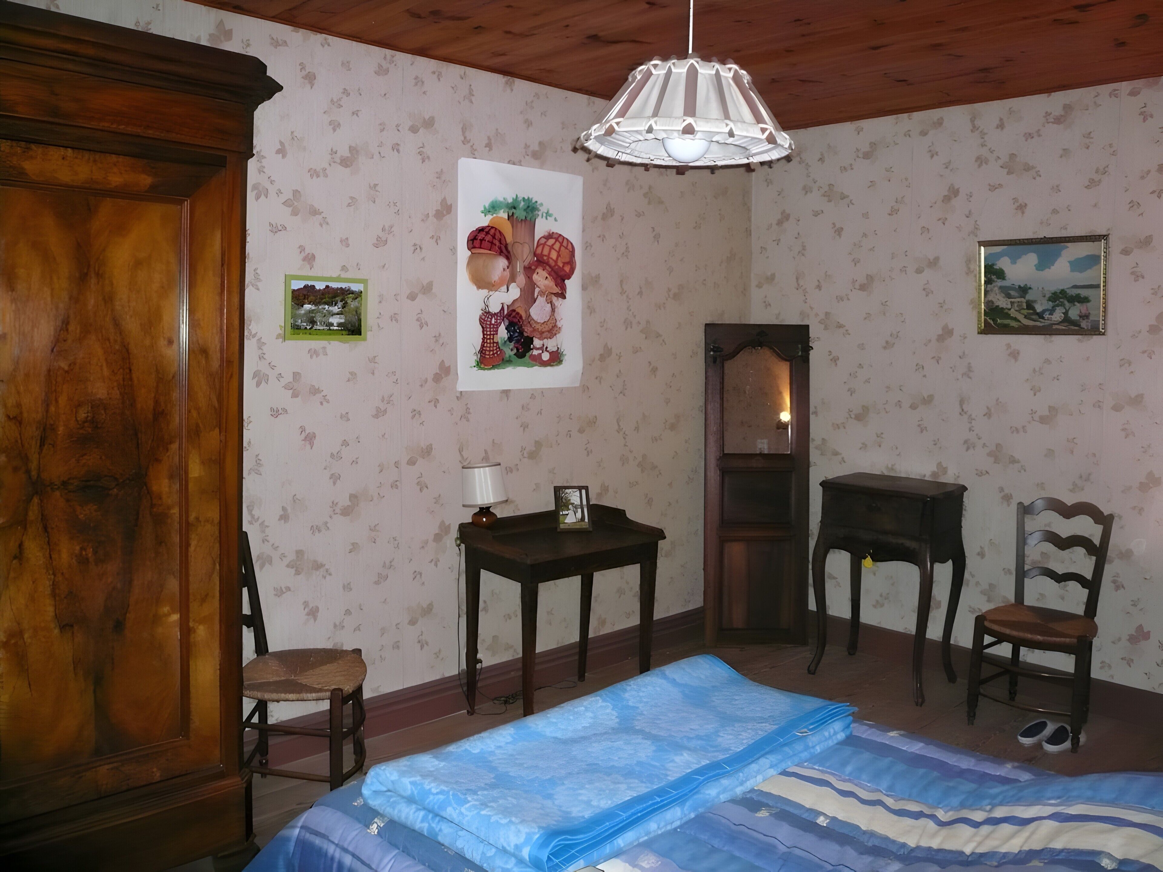 Une pièce comprenant un lit, une armoire en bois, un bureau, une chaise et une lampe suspendue.