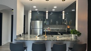 Una cocina moderna con una isla central, taburetes negros y luminarias colgantes.
