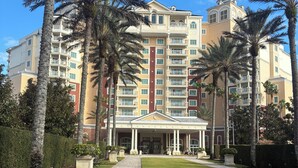 Un hotel de varios pisos con un patio central, palmeras y un césped bien cuidado.