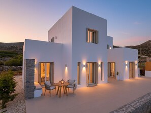 A modern two-story building with a flat roof, large windows, and a patio area with outdoor seating. - Villa Darros (Agkeria)