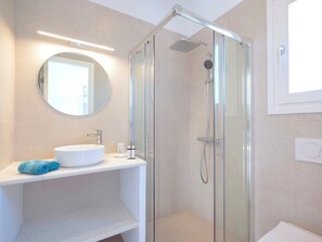 A modern bathroom with a glass-enclosed shower, a round mirror, and a white sink with a blue towel. - Villa Darros (Agkeria)