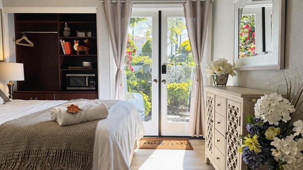 A bedroom with a bed, a wardrobe, a dresser, a mirror, and a window with curtains. - Elegant Designer Suite: Serene Garden View & Private Entry (Escondido)
