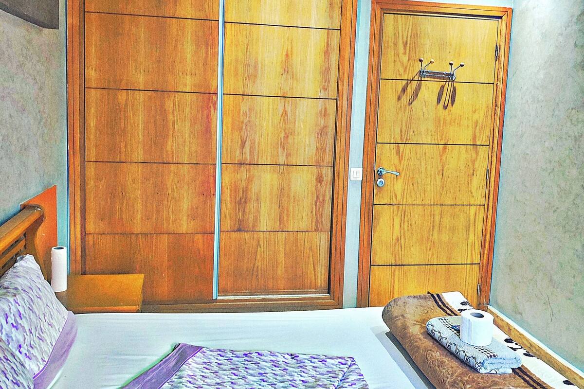 Un dormitorio con cama, mesita de noche, armario de madera y baño con inodoro.