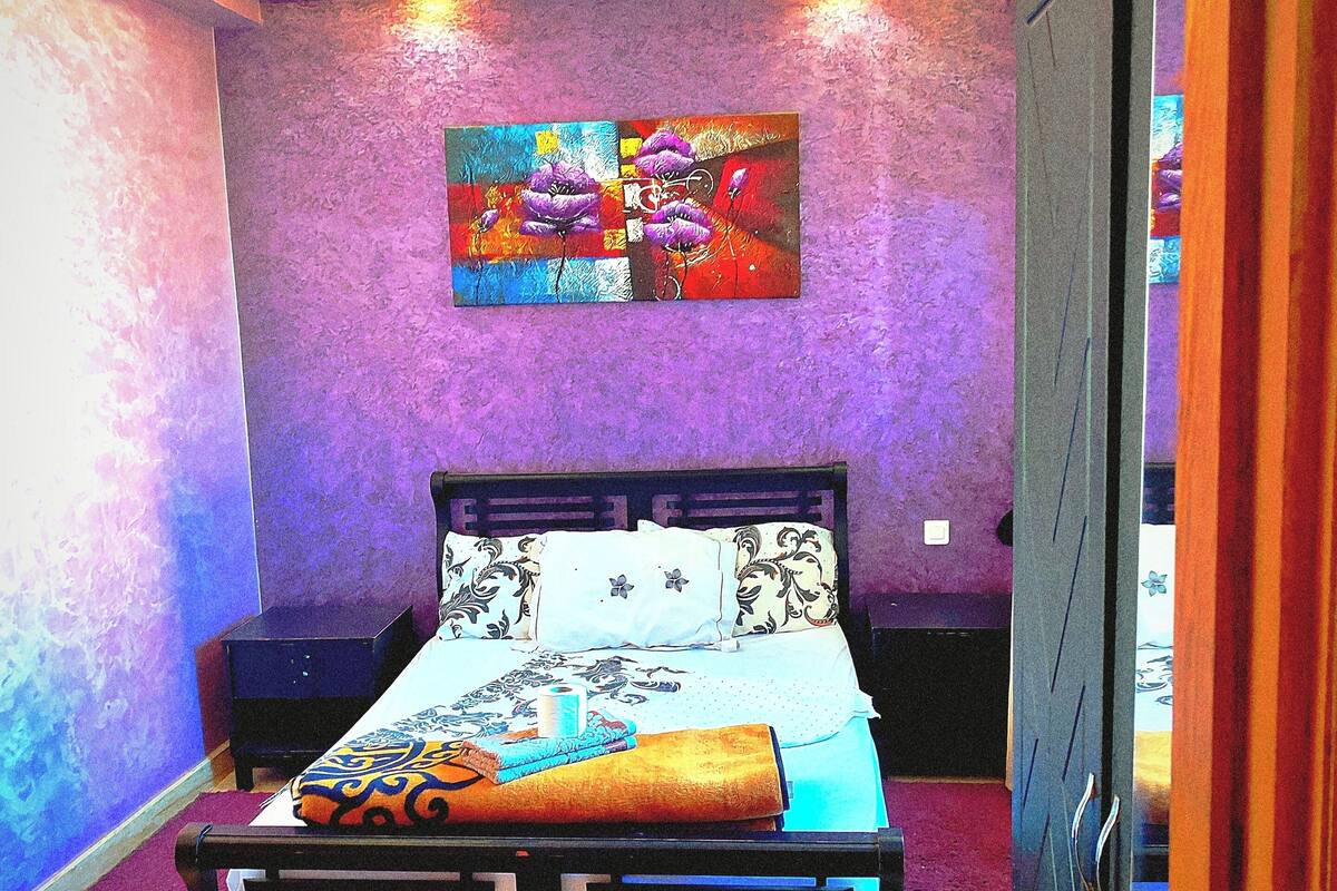 Un dormitorio con una cama, una mesita de noche, un cuadro y una puerta.
