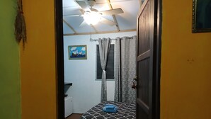 Ein Zimmer mit einem Bett, einem Deckenventilator, einem Fenster mit Vorhängen und einem Bild an der Wand.
