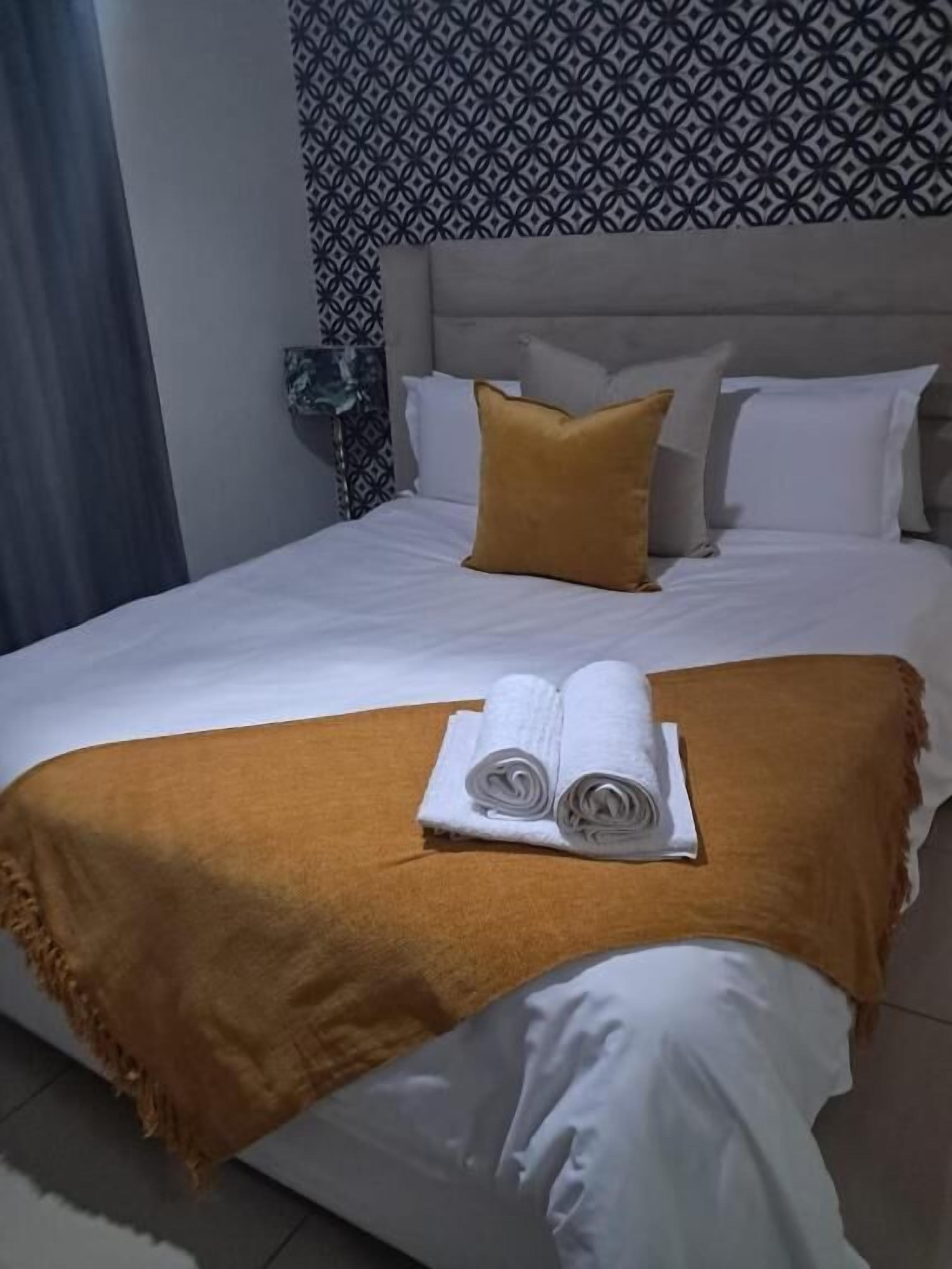 Un lit bien fait, avec des draps blancs, un plaid marron et deux serviettes enroulées posées sur le lit.
