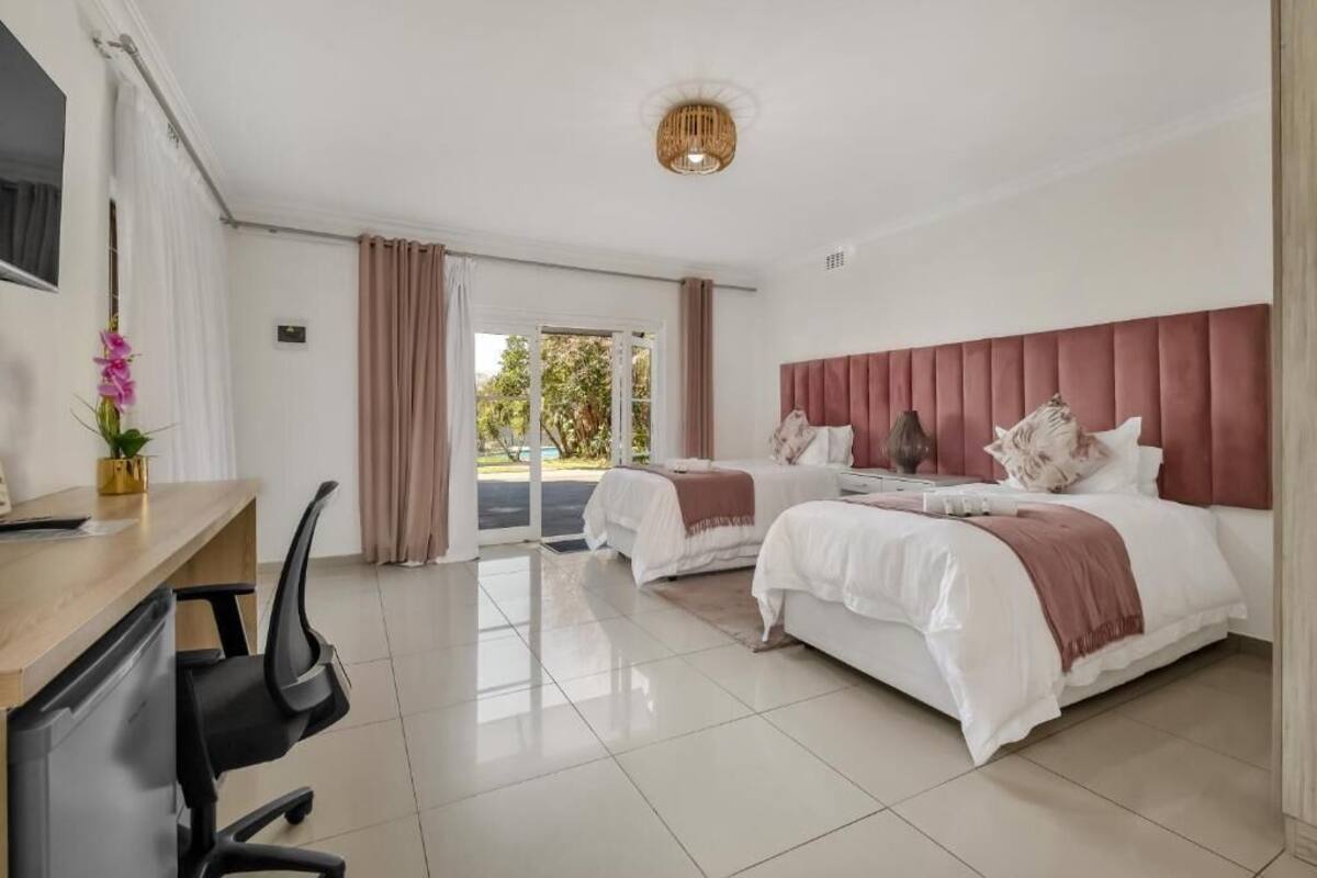 A hotel room with two beds, a desk with a chair, a television, and a view of the outdoors.