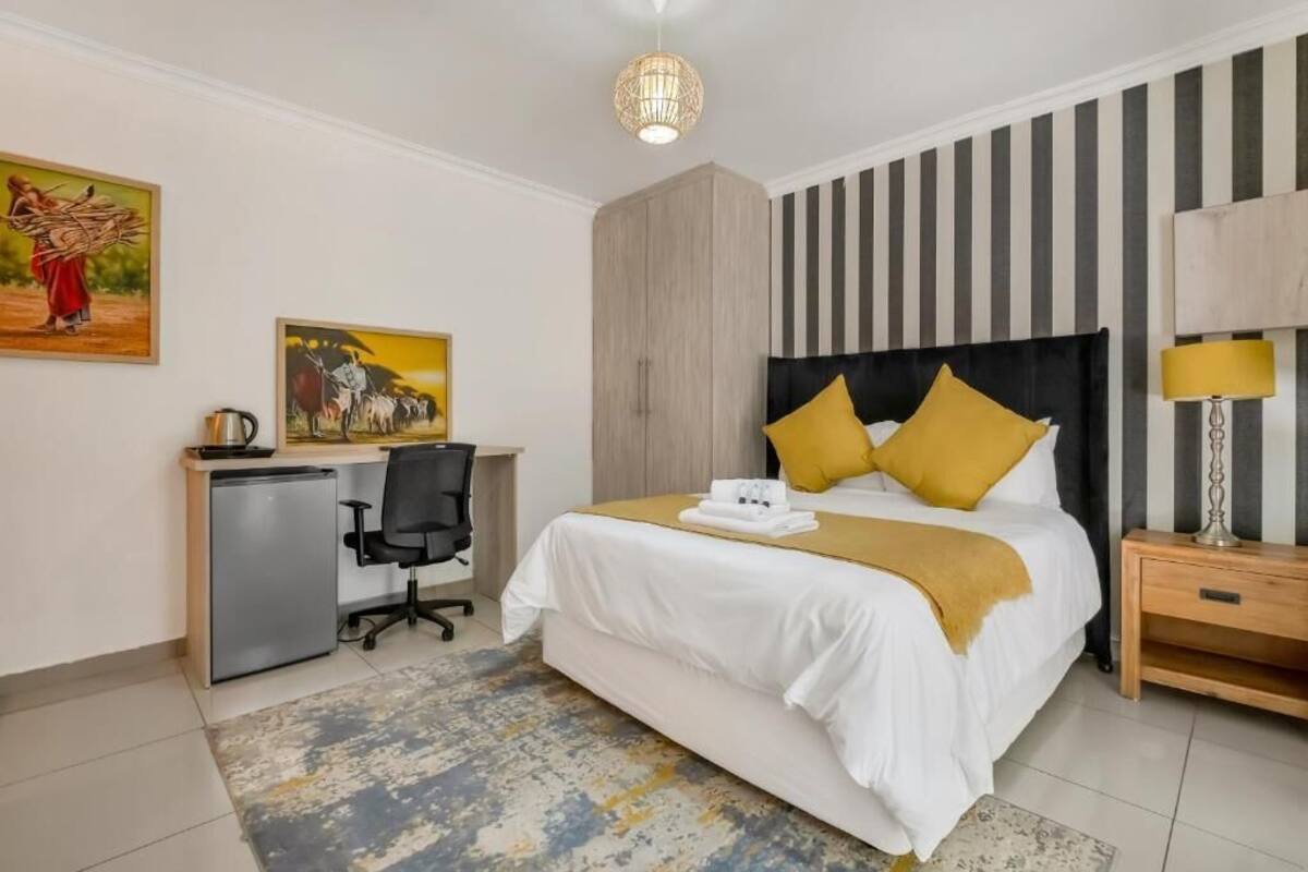 A hotel room with a bed, a desk, a chair, a wardrobe, and a lamp.