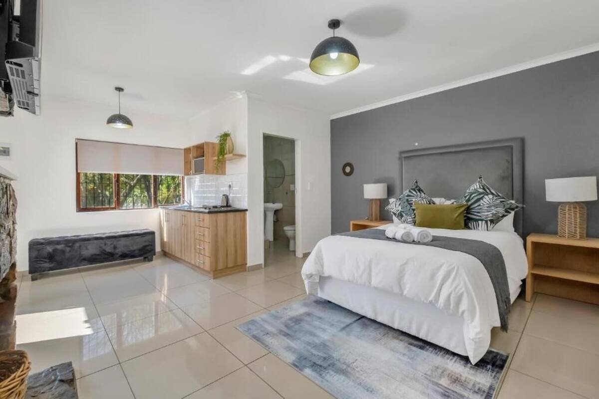 A modern bedroom with a large bed, bedside tables, a bench, and a view of the bathroom.