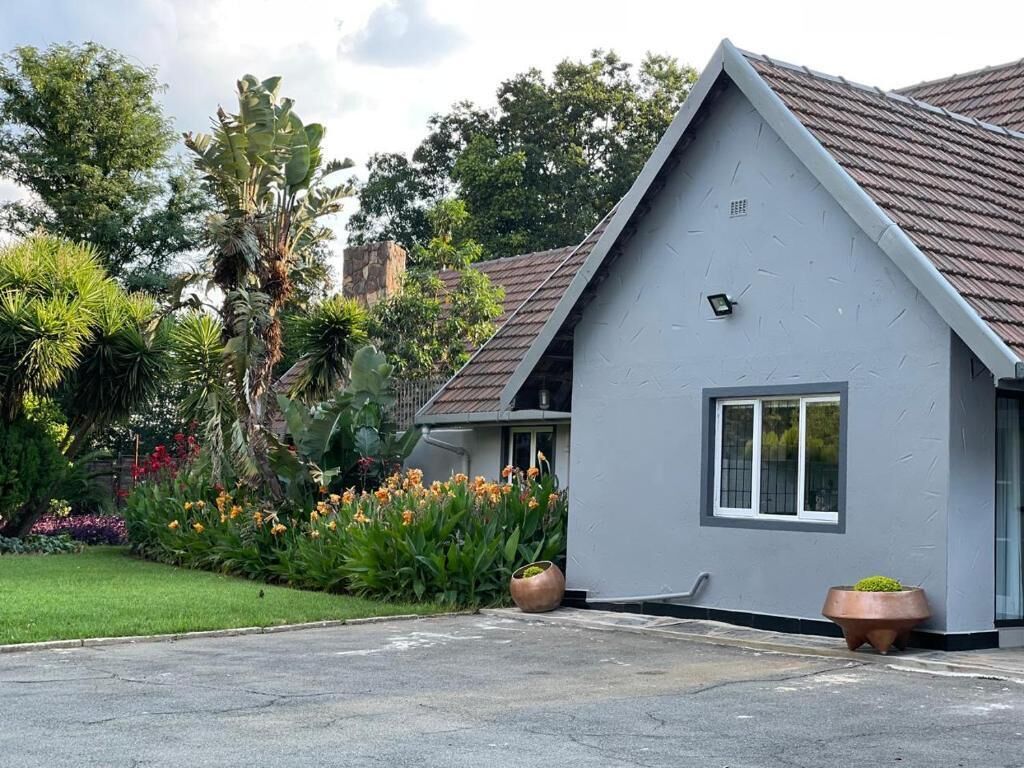 A modern house with a grey facade and a sloped roof, surrounded by lush greenery and flowering plants.