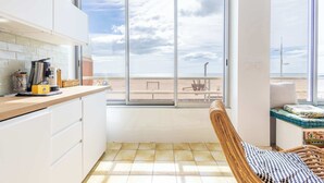 Eine Küche mit einem großen Fenster, einem Korbstuhl und Blick auf den Strand.