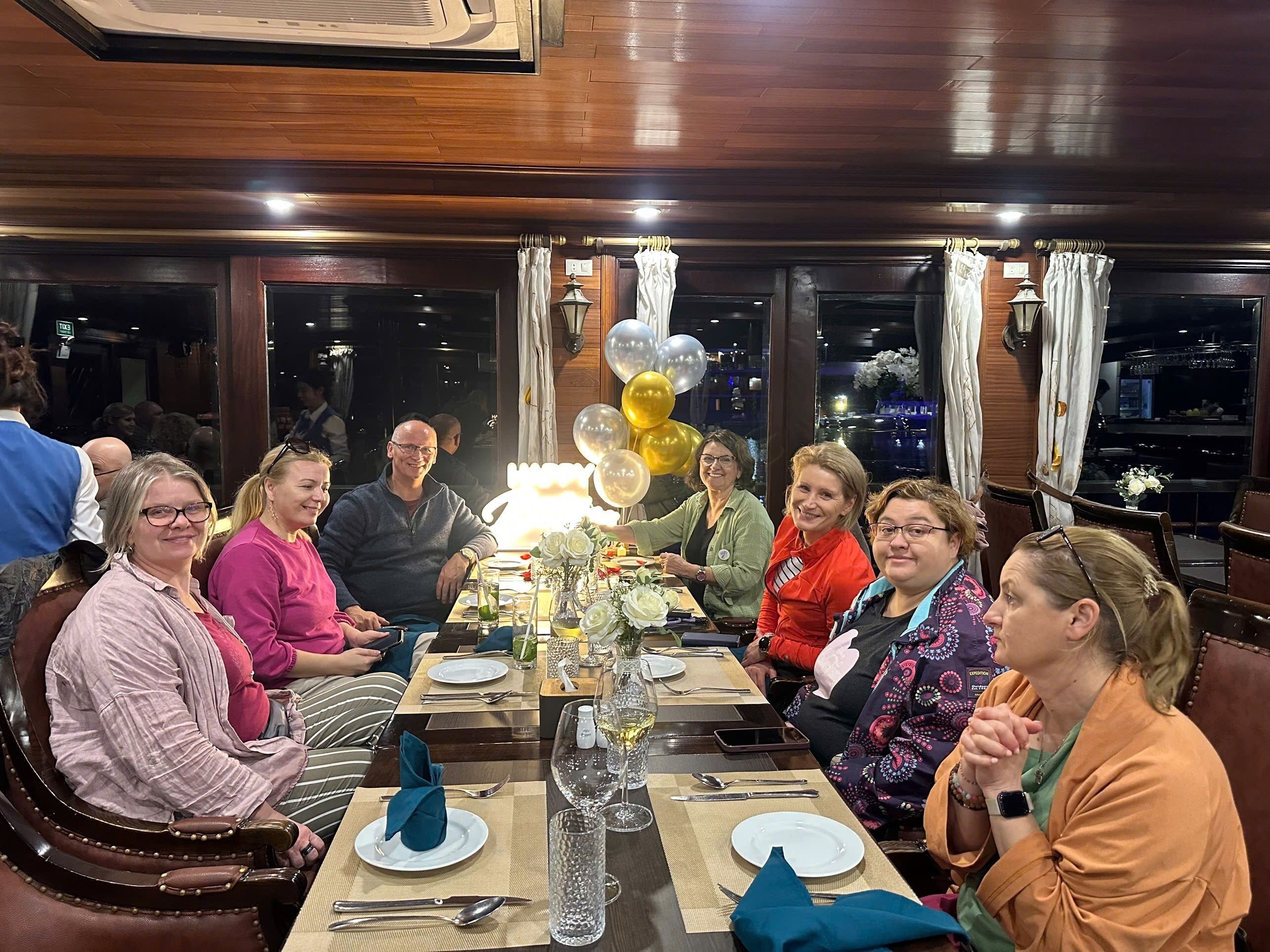 A group of people seated around a table with a city view, balloons, and a candle centerpiece.