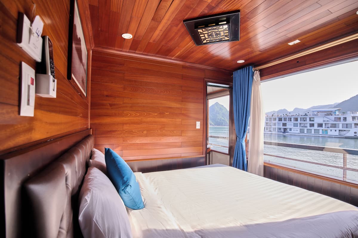 Una habitación con techo de madera, cama con ropa blanca y vista a un río con edificios al fondo.
