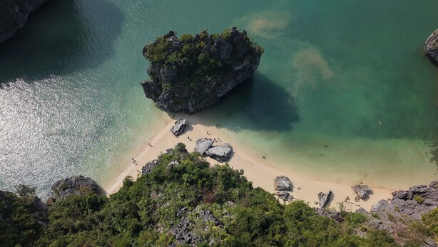 Eine Küstenlandschaft mit einem Felsen, umgeben von klarem türkisblauem Wasser und einem Sandstrand.