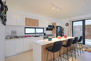 A modern kitchen with a central island, bar stools, and a large window. - Trou aux Biches Rooftop Jacuzzi - 3 bed ensuite (Pamplemousses District)