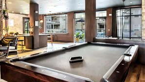 A pool table in a modern indoor setting with large windows and a bar area. - Boulevard Stays Dashing King 1 BR Suite Pool, Parking Gym M (Richardson)