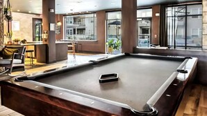Ein Billardtisch in einem modernen Innenbereich mit großen Fenstern, einer Bar und Sitzgelegenheiten.