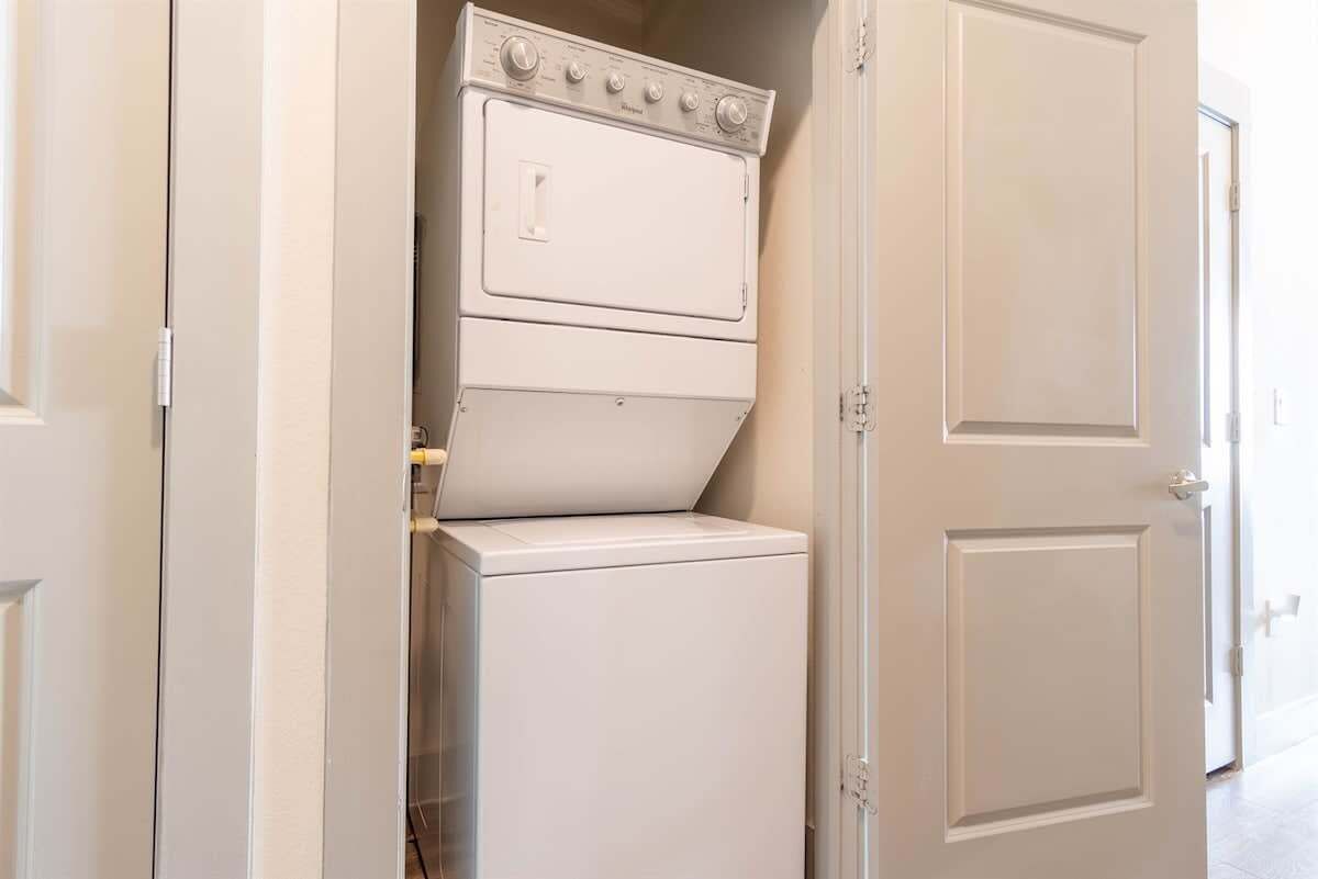 Une petite buanderie équipée d’un lave-linge et d’un sèche-linge superposés, d’une porte et d’un couloir.