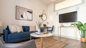 Ein modernes Wohnzimmer mit einem blauen Sofa, einem runden Couchtisch, einem Fernseher und einem Topf mit Pflanze.