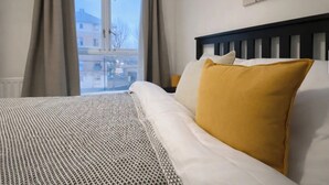 Quarto de hotel com cama, janela com cortinas e um quadro na parede.