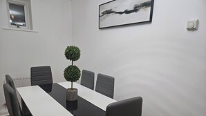 Uma sala de conferências com uma mesa branca, seis cadeiras e duas plantas em vasos.
