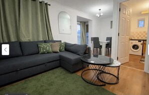 Ein modernes Wohnzimmer mit einem grauen Ecksofa, einem runden schwarzen Couchtisch und einem grünen Teppich.