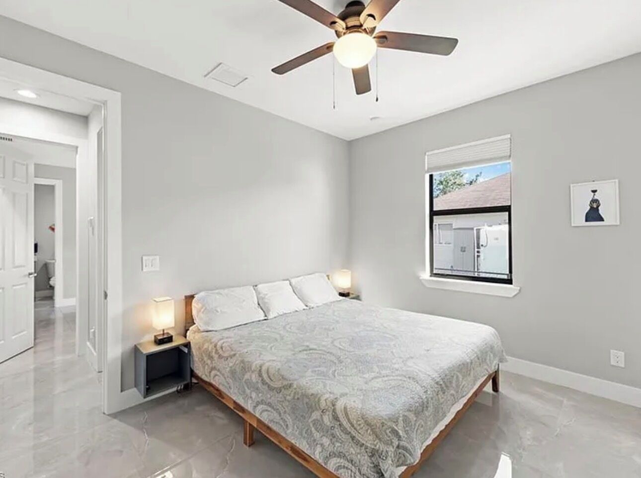 A bedroom with a bed, nightstands, a ceiling fan, a window, and a door.