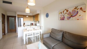 A modern living room with a sofa, a dining area with chairs, and a kitchen in the background. - Apartment Panoramic B4 by Parc Mont-roig (Miami Playa)