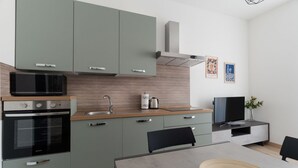 Eine moderne Küche mit Mikrowelle, Backofen und Spüle. Ein Esstisch mit Stühlen und ein Flachbildfernseher sind vorhanden.