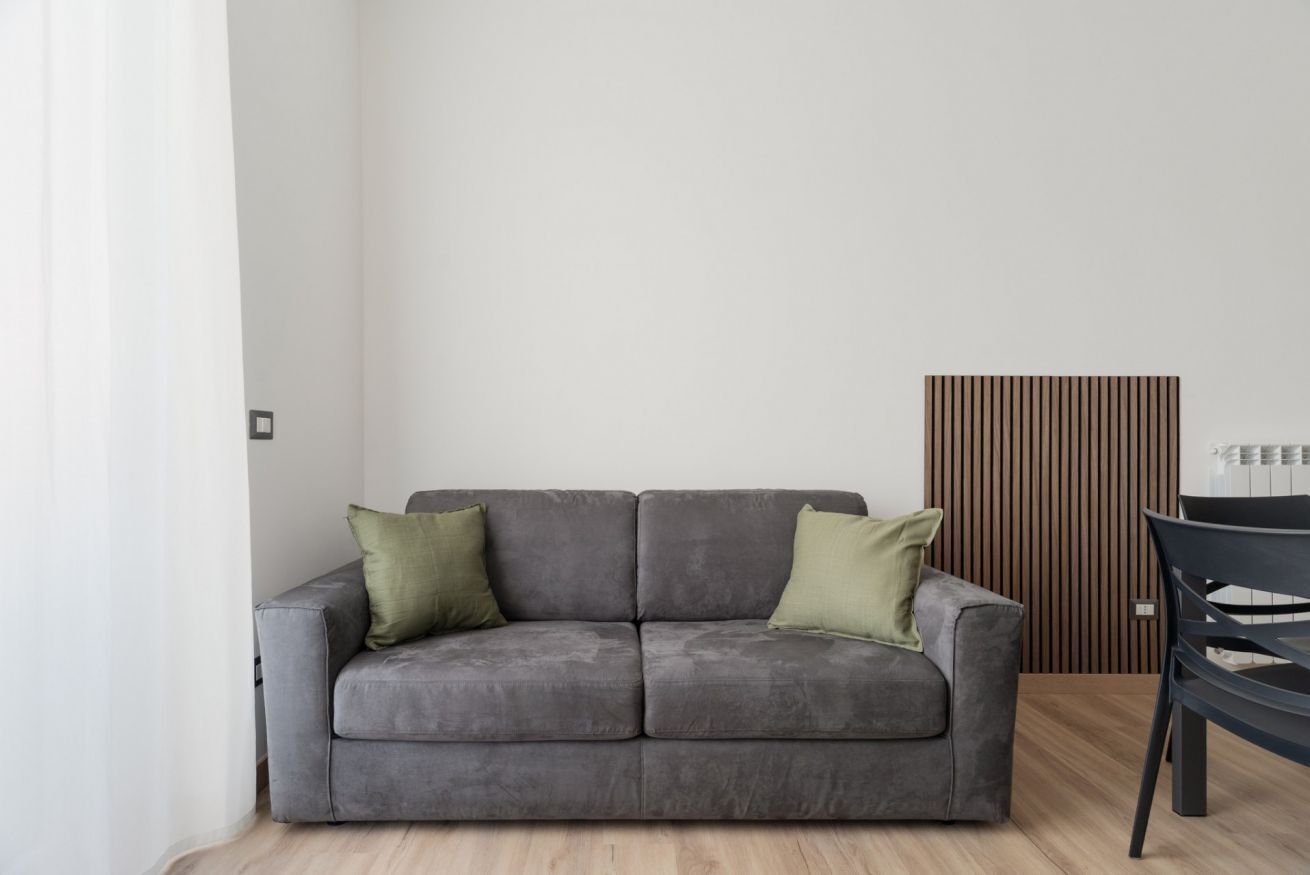 A grey sofa with two pillows, a wooden slat wall, and a black chair.