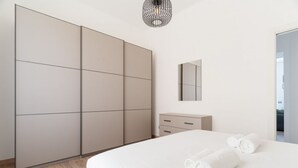 Ein modernes Schlafzimmer mit einem großen Bett, einem Kleiderschrank, einer Kommode und einem Spiegel.
