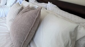 Ein ordentlich gemachtes Bett mit weißer und gemusterter Bettwäsche, einem Holz-Kopfteil und gerahmten Bildern an der Wand.