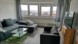 Un saló modern amb un sofà gris, una taula de centre de vidre i un televisor de pantalla plana sobre un suport de fusta.