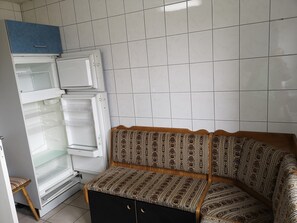 A compact living space with a built-in refrigerator, a bench with patterned upholstery, and a tiled wall.